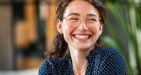 Portrait of laughing young woman wearing spectacles in office. Carefree casual girl wearing glasses and looking away. Confident beautiful student wearing specs and smiling.