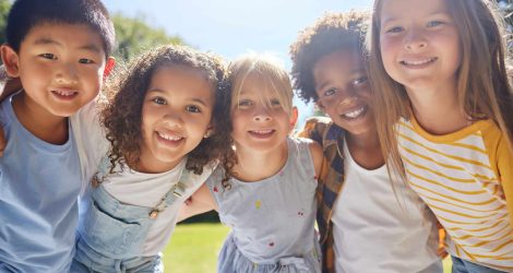 Happy, smile and portrait of kids in a park playing together outdoor in nature with friendship. Happiness, diversity and children friends standing, embracing and bonding in a outside green garden