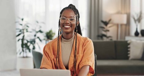 Black woman, portrait in home office and laptop for remote work, social media or blog research with smile in apartment. Happy freelancer at desk with computer for email, website or online in house